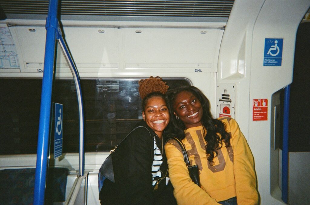 Two Black girls posing for a picture smiling in the Tube in London.