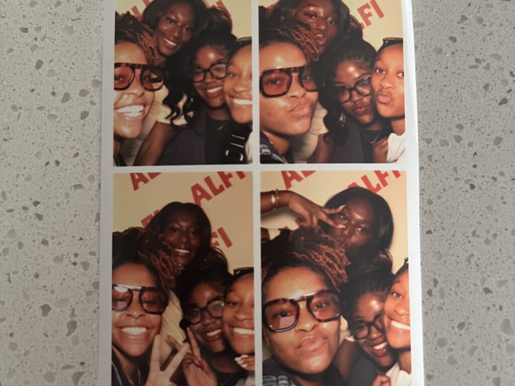 Four Black girls posed in a photo booth picture making silly faces.