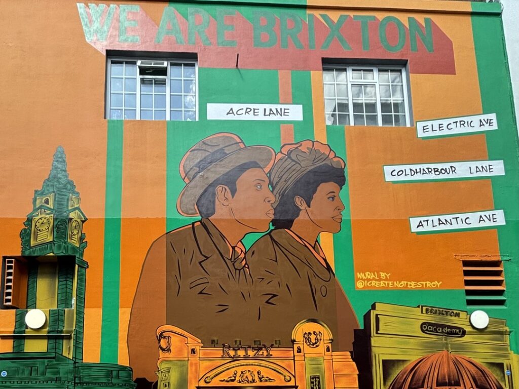 Mural in Brixton, London. Mural the colors orange and green, showing a Black man and woman posed next to landmark in Brixton.
